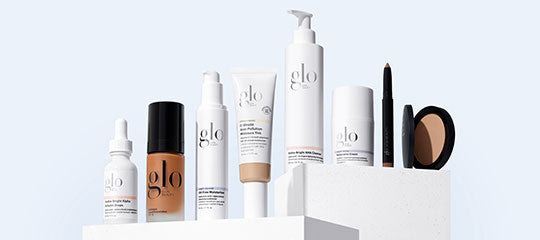 Assorted glo skincare and makeup products—bottles, pump, tube, pencil, and compact—displayed on white pedestals.