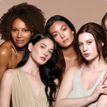 Four diverse women with different skin tones and hair styles posing closely together against a neutral background