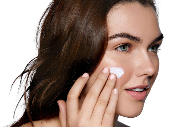 Young woman applying white facial cream to her right cheek, close-up of face and hand